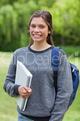 Smiling teenage girl holding a notebook while standing in a park