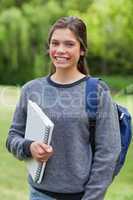 Smiling teenage girl holding a notebook while standing in a park