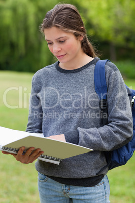 Young woman reading her notebook while standing up in a park