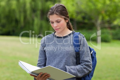 Young serious woman reading her notebook while standing in a par