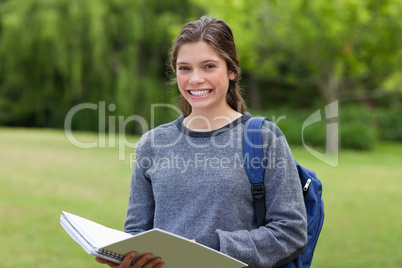 Young happy girl holding her notebook in a park while showing a