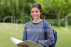 Young happy girl holding her notebook in a park while showing a