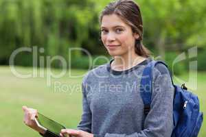 Smiling young woman holding a tablet pc while standing in a park