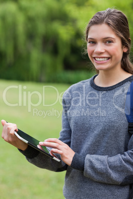 Smiling student using her tablet pc while standing in a park
