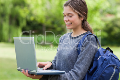 Young smiling woman holding her laptop while carrying her backpa