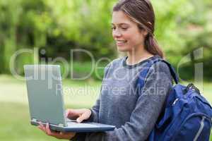 Young smiling woman holding her laptop while carrying her backpa