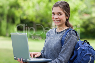 Happy young girl holding her laptop while smiling in front of th