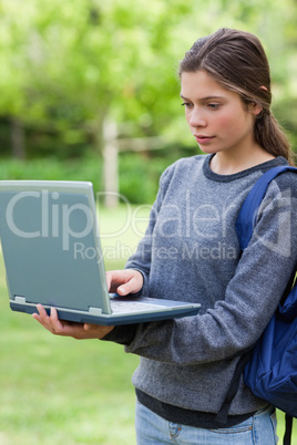 Serious student typing on her laptop while standing upright in a