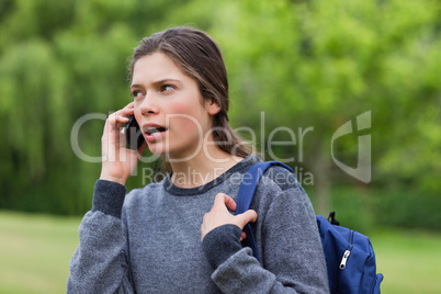 Young calm girl talking on the phone while looking towards the s