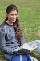 Smiling young adult holding an open book while sitting on the gr