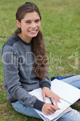 Smiling young woman writing on her notebook while looking at the
