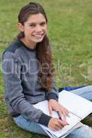 Smiling young woman writing on her notebook while looking at the
