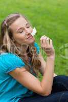 Young smiling woman closing her eyes while smelling a flower
