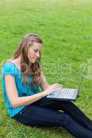 Young relaxed woman using her laptop while sitting on the grass