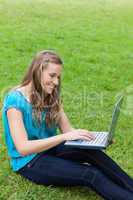 Young smiling girl typing on her laptop while sitting down on th