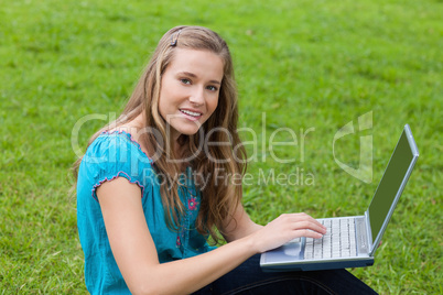 Young girl using her laptop in a park while looking at the camer
