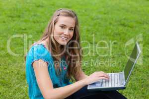 Young girl using her laptop in a park while looking at the camer