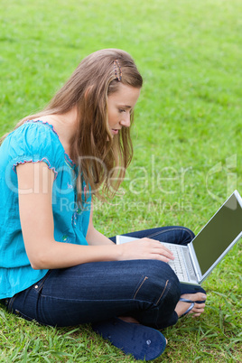 Young serious girl sitting cross-legged in a park while using he