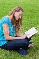 Serious young girl reading a book while sitting in a park