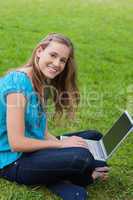 Young smiling girl looking at the camera while using her laptop