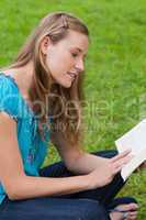 Young attractive girl sitting cross-legged in a park while readi