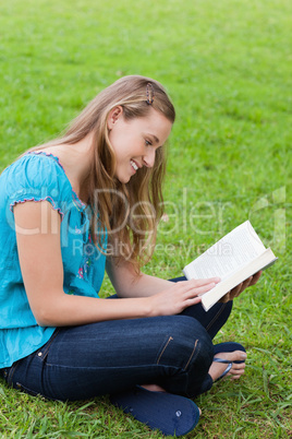 Happy young girl reading a book while sitting down in a park