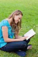 Happy young girl reading a book while sitting down in a park