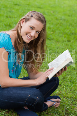 Young smiling woman looking at the camera while reading a book