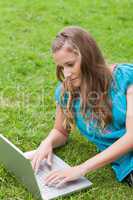 Young serious girl lying on the grass while using her laptop