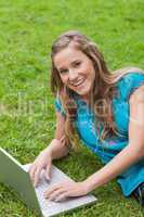 Smiling teenage girl lying on the side while using her laptop