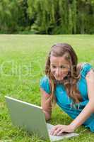 Smiling teenager lying in a park while typing on her laptop