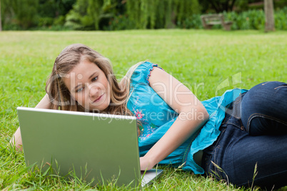 Smiling teenager lying on the grass with her hand on head while