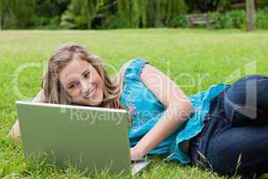 Young smiling girl lying on the side in a park while typing on h