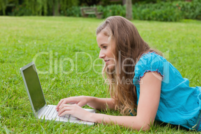 Side view of a young girl typing on her laptop while lying down