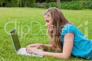 Side view of a young girl typing on her laptop while lying down