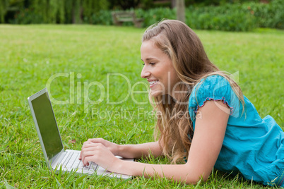 Young smiling girl looking at her laptop while lying down