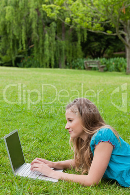 Side view of a young girl working on her laptop while lying on t