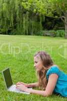 Side view of a young girl working on her laptop while lying on t