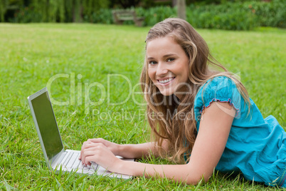 Smiling teenager using her laptop while lying down in a park