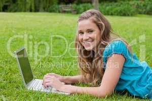 Smiling teenager using her laptop while lying down in a park