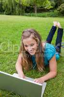 Smiling student working on her laptop in a park while lying with