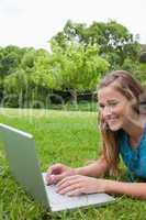 Young smiling girl using her laptop in a park while lying on the