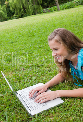 Smiling young woman lying in a park while working on her laptop