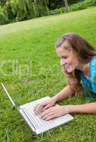Smiling young woman lying in a park while working on her laptop