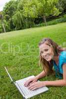Smiling girl lying in a public garden while working on her lapto