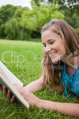 Young girl reading a book in a parkland while laughing