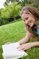 Young smiling woman reading a book while lying in a parkland