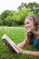 Young smiling woman lying in a parkland while holding a book