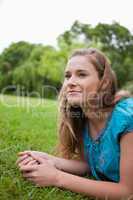 Thoughtful young girl looking away while lying on the grass