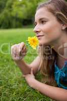 Young girl lying on the grass while smelling a flower